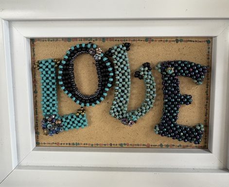 LOVE A white box frame containing beaded letters in stunning shades of blue to spell out the word LOVE.